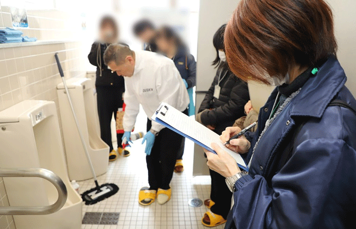 トイレ清掃についてレクチャーを受ける見学者の画像